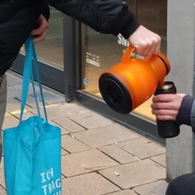 Eine Kanne schenkt Wasser in einen Becher ein